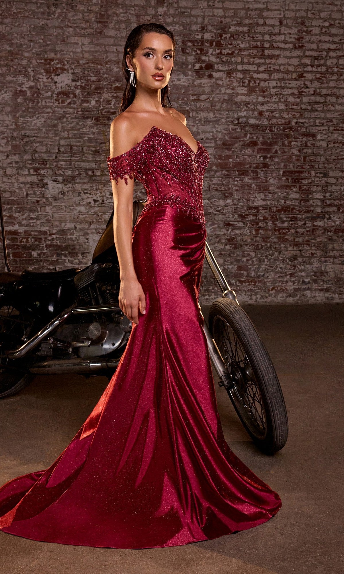 A woman in the Ladivine CC456 Off-Shoulder Long Gold Prom Dress stands beside a motorcycle against a brick wall backdrop.